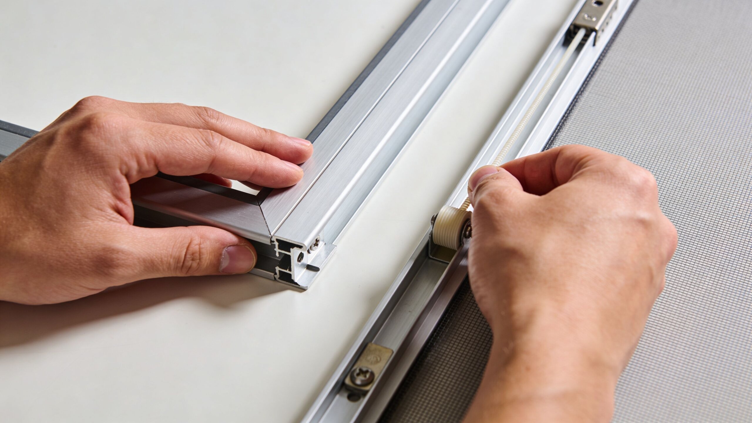 Hands carefully assembling a custom window screen frame using aluminum profiles and specialized screen hardware components.