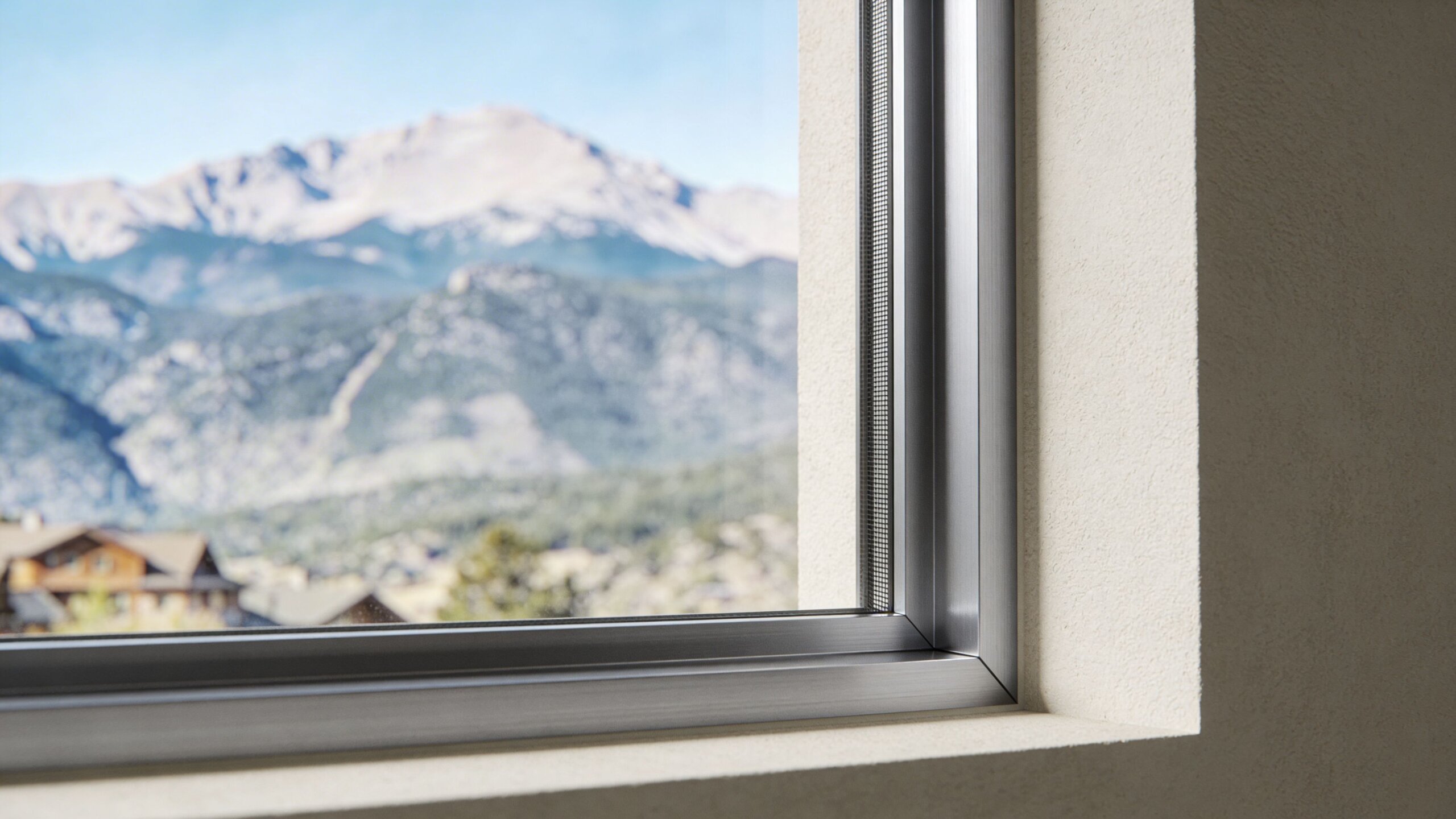A close-up view of a modern silver aluminum window frame with a mesh screen overlooking mountains.