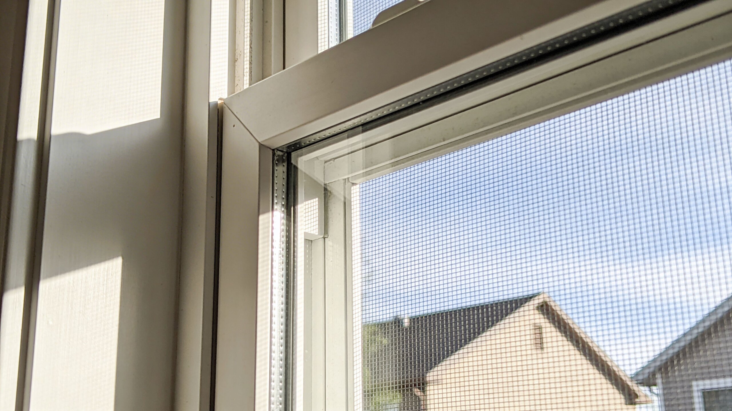 Close-up view of a white vinyl window frame with a screen mesh looking out towards houses.