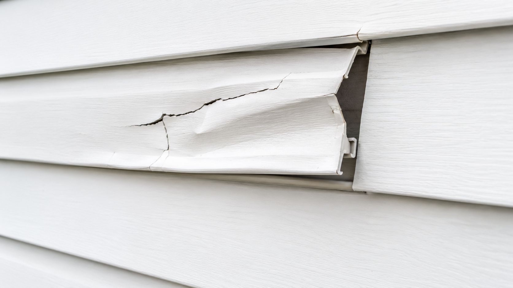 A close-up view of damaged white vinyl house siding that has cracked and melted from heat.