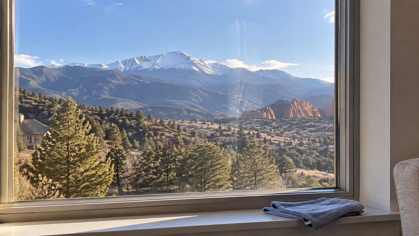 A scenic view of snow-capped mountains and red rock formations seen through a clear glass window.